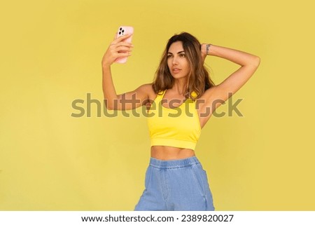 Pretty brunette woman posing with mobyle phone  over yellow background. Casual stylish outfit.  