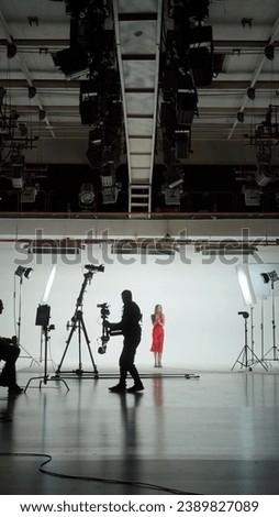 Professional filming pavilion with a white cyclorama. Shooting of a girl in a red dress who sings into a retro microphone. Director, Cameraman and crew in Backstage.