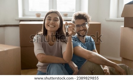 Young couple sit on floor near heap of carton boxes with personal stuff smile look at camera showing keys from their new bought or rented flat, start independent life together. Tenancy, cohabitation Royalty-Free Stock Photo #2389829855