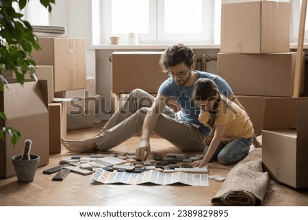 Young father and little daughter sit on floor choosing samples for house decoration, review colorful swatches start renovation of new apartment. Relocation of young family to own flat, repair works
