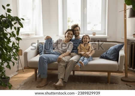 Young happy family sit on sofa in living room looking at camera, pose, spend weekend time together. Caring spouses enjoy friendly relationship, express love and tenderness. Unity, parenthood, devotion Royalty-Free Stock Photo #2389829939