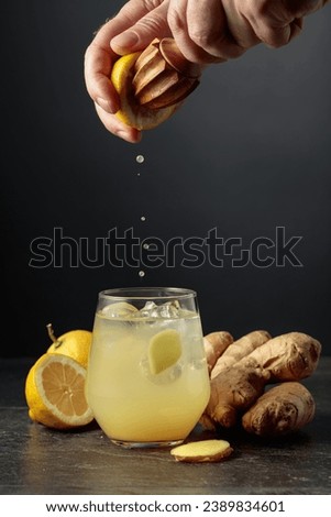 Ginger Ale with ice and lemon. Juice is squeezed out of a lemon with an old wooden juicer. Royalty-Free Stock Photo #2389834601