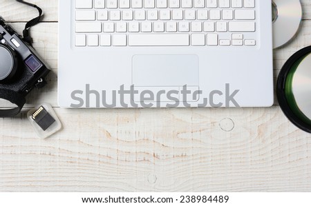High angle shot of a digital photography workspace. The closeup includes a computer keyboard, CD's, memory card, and digital camera. Horizontal format with copy space, on a white rustic table.