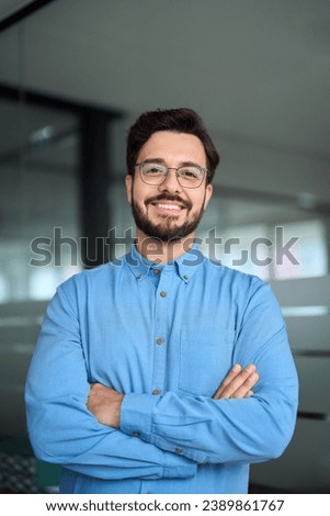 Happy young latin business man leader looking at camera standing arms crossed in office hallway. Successful businessman manager, smiling professional executive or male entrepreneur, vertical portrait.
