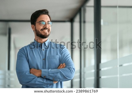Confident young latin business man leader looking aside standing in office hallway. Happy businessman manager, smiling professional company executive thinking of financial success ideas concept. Royalty-Free Stock Photo #2389861769