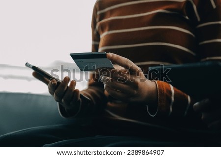 A credit card in the hands of a young businesswoman pays for a business on a mobile phone and on a desk with a laptop.