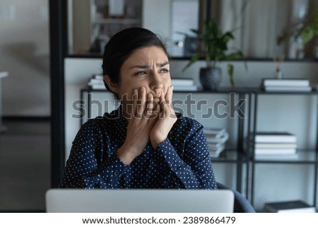 Upset frustrated young Indian student girl working at laptop, looking away thinking over bad news, feeling toothache, stress. Employee concerned, worried about problems with computer Royalty-Free Stock Photo #2389866479
