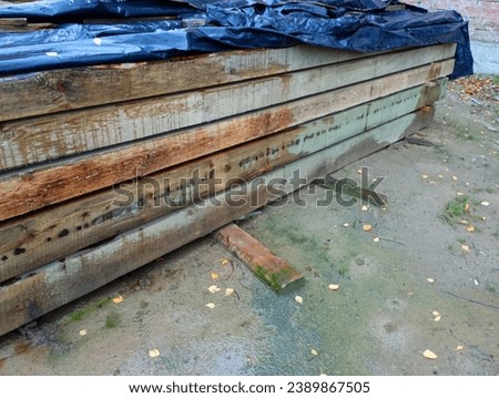 Stacked wooden beams on a construction site. The material for covering the house is neatly folded.