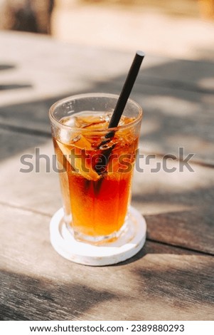 A glass of cool tea with ice and a paper straw on a wooden table