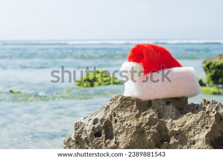 Santa Claus' red hat on a stone on the background of the ocean. Stylish Christmas Holidays and Vacation Concept