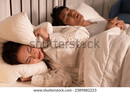 Night time Asia woman annoying and cover her ears with pillow of boyfriend snoring on bed  Royalty-Free Stock Photo #2389882223