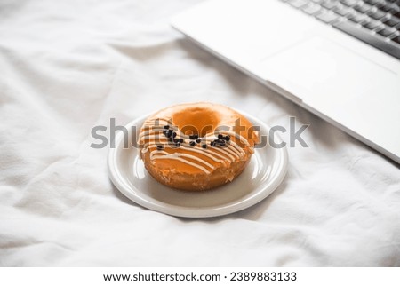 Orange donut and laptop in white bed, home office, breakfast in bed.
