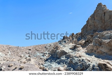 Surroundings of Teide. Volcano located on the Spanish island of Tenerife, you can see the inhospitable terrain, blue sky, large rocks of volcanic origin and typical vegetation. Royalty-Free Stock Photo #2389908329