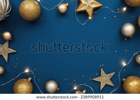Christmas frame border with golden balls, stars, ribbon on blue background, flat lay