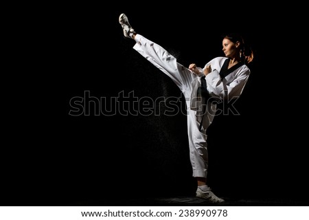 Young woman giving a kick on black background