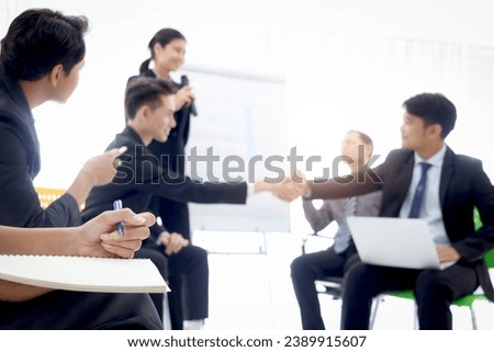 Businesswoman hand holding a pen ready for taking note at the meeting with blurred background of businesspeople group at conference. Secretary officer taking minutes for making a report.  Royalty-Free Stock Photo #2389915607