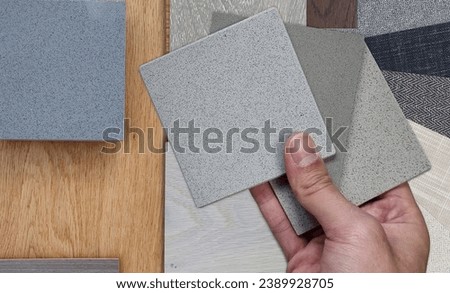 designer holds quartz samples palette to compares with wooden engineering flooring tiles, stone and concrete tiles, fabric laminated. mood board shows various type of material samples, close up view. Royalty-Free Stock Photo #2389928705