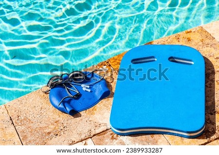 top view, medium distance of, competitive swimming equipment, kick board, goggles, ear pluges and swim cap, pool side Royalty-Free Stock Photo #2389933287