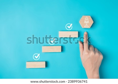 Hand with rocket and checklist icon on wooden blocks for successful business goal achievement, Rocket ship launching for business planing and development, Ladder for success