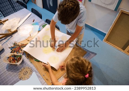 Overhead view of kids holding pencils and drawing on white paper sheet in creative art workshop. Creativity and art skills development concept. Kids and education