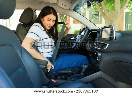 Mexican beautiful young woman putting on the seat belt before driving the car and going for a trip or travel  Royalty-Free Stock Photo #2389965189
