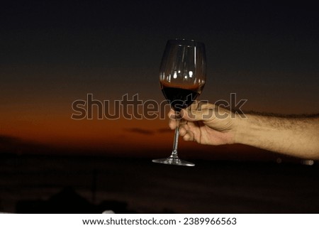 Romantic dinner, glass of red wine held by a man's hand, with the sunset in the background