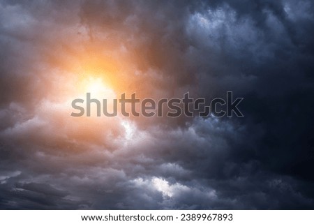 Epic dramatic storm sky with sun. Dark grey blue cumulus rain clouds with orange yellow light and sunlight, thunderstorm