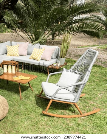 Sunny Outdoor Retreat, Modern Patio Sectional Sofa Adorned with Patterned Yellow Cushions, a Sleek Grey Rocking Chair, Mid-Century Wooden Side Table, Set Against a Backdrop of Lush Palm Trees, Spring.