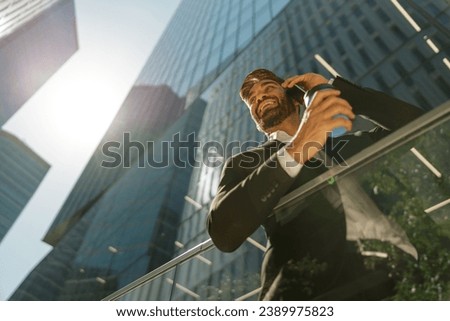 Smiling businessman is talking phone and drinking coffee standing on background of city skyscrapers