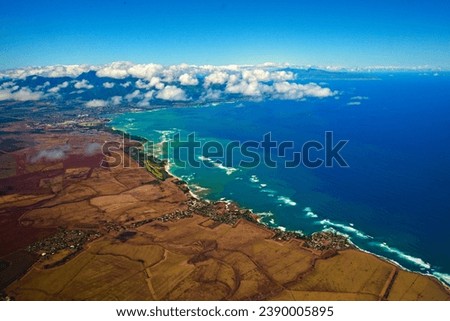 The Hawaiian island of Kauai, as seen from an island-hopping airplane. Fluffy white clouds contrast with the turquoise waters of the Pacific Ocean. High quality photo Royalty-Free Stock Photo #2390005895