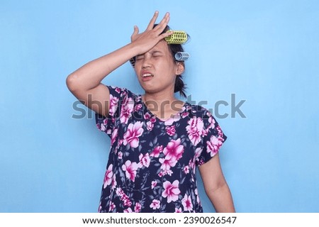 Upset Asian housewife wear hair curlers slapping forehead with palm and showing worried or regret expression Royalty-Free Stock Photo #2390026547
