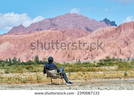 rear view of asian man sitting in chair on riverbed looking at canyon cliffs in Kuche, Xinjiang, China Royalty-Free Stock Photo #2390087133