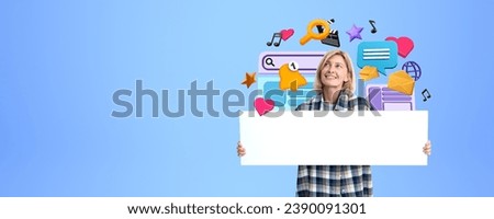 Happy young woman showing mockup blank signboard, looking up at colorful cartoon social media and internet icons on copy space blue background. Concept of communication and message