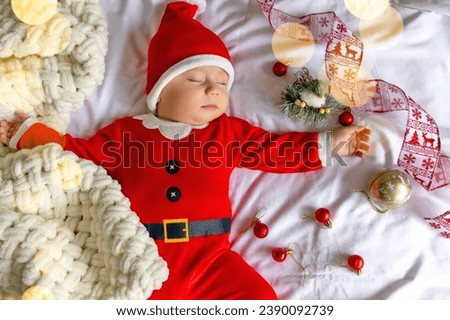 Cute little baby in Santa hat and red clothes costume sleeping at home.