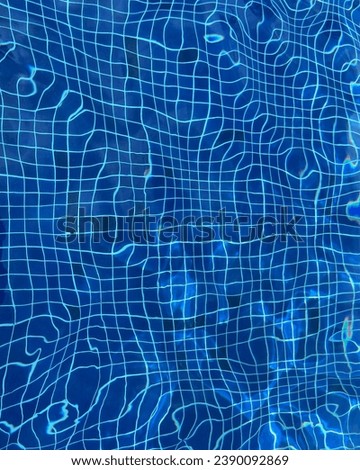 Top view photo of a detail of a swimming pool water with the blue tiles distorded by the motion and wavy waves of the liquid that twist the white lines of the ground deep floor of the pool