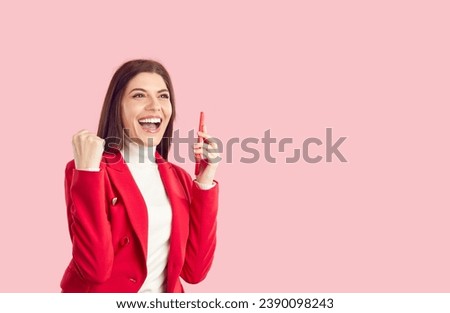 Portrait happy joyful excited beautiful business woman in red suit on solid pastel pink empty blank copy space studio background, holding phone, celebrating winning good deal and shouting Yes, Hooray