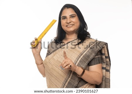 Indian school teacher showing finger with scale while standing isolated in white background. looking in front of the camera
