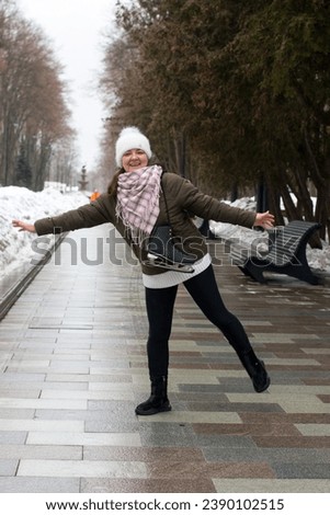 A woman walks in a winter park with skates on her shoulder. Coming from training