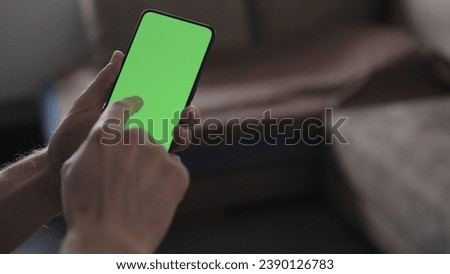 Man use smartphone with green screen while standing in living room