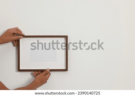 Young man hanging picture frame on white wall indoors, closeup