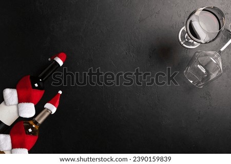 Glasses and bottles with red and white wine wearing Santa Claus hat and scarf on black background. Christmas celebration. New year decoration
. Flat lay
