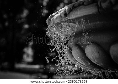 A black and white photograph of a fountain with a beautiful ornament from which water drips in a cascade on a sunny day.