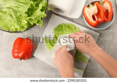 Woman wiping lettuce with paper towels at grey table, top view Royalty-Free Stock Photo #2390185201