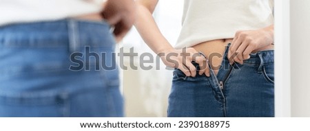 Diet motivation concept, Stressed Young woman trying to zip up her jeans and feel tight after weight gain in front of mirror at home. Royalty-Free Stock Photo #2390188975