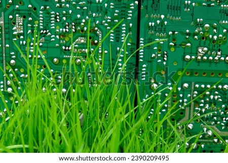 An image showing a green circuit board with numerous small components, set against a backdrop of grass.