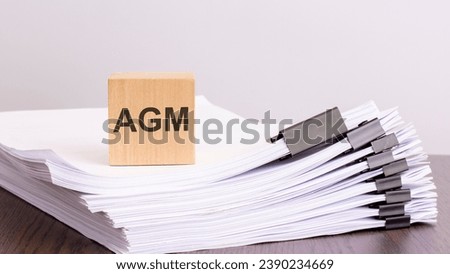 a wooden block with a text AGM on a stack of documents. brown table, gray background Royalty-Free Stock Photo #2390234669
