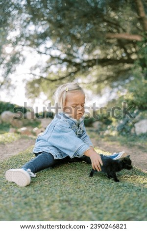 Little girl with a tiny black kitten sits on a green lawn