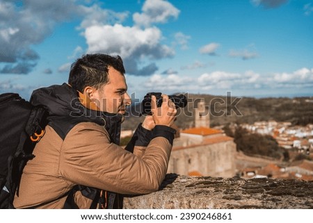 portrait of young man photographer, photographing a town traveling with his backpack and camera sightseeing, seen from the side