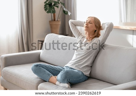 Relaxation in living room at home. Calm woman sitting on couch and holding hands behind head. Female with closed eyes leaning back, enjoying free time weekend, taking nap