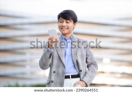 Korean Young Business Man Using Voice Search App Holding Cellphone Near Mouth And Talking, Utilizing Mobile Assistant Service Standing Outdoors In Urban City Area. Online Communication